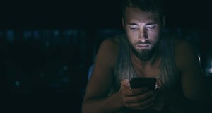 Person sitting in the dark looking at their smart phone
